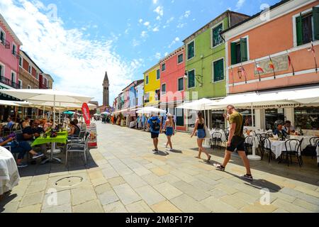 BURANO ISLAND, VENEDIG, ITALIEN - 4. JULI 2022: Touristen unter den souveränen Geschäften und Restaurants auf der Hauptstraße der insel burano, bunte Häuser Stockfoto