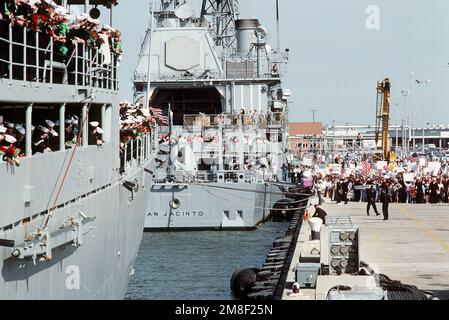 Die Besatzungsmitglieder beobachten vom Geländer des nuklearbetriebenen Führungsraketenkreuzers USS MISSISSIPPI (CGN-40) aus, wie Mitglieder der wartenden Menge nach der Ankunft des Schiffs im Hafen den Führungsraketenkreuzer USS SAN JACINTO (CG-56) besteigen. Schiffe des Flugzeugträgers USS JOHN F. KENNEDY (CV-67) kehren nach Norfolk zurück, nachdem sie während der Operation Desert Storm im Persischen Golf stationiert waren. Betrifft Operation/Serie: STÜTZPUNKT WÜSTENSTURM: Marineflugstation, Norfolk Bundesstaat: Virginia (VA) Land: Vereinigte Staaten von Amerika (USA) Stockfoto