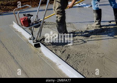 Beim Bau einer neuen Einfahrt wird die Maschine verwendet, um frischen Beton auf der obersten verdichteten Schicht auszurichten Stockfoto