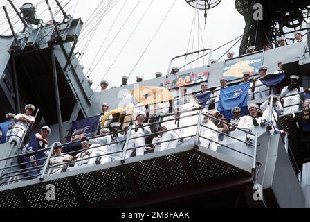 Offiziere und Soldaten an Bord des Flugzeugträgers USS AMERICA (CV-66) stehen in der Nähe der Schiffsbrücke und blicken über die Menge, die sich am Pier versammelt hat, um sie zu begrüßen. DIE USA kehren nach Norfolk zurück, nachdem sie für Operation Desert Shield und Operation Desert Storm im Persischen Golf eingesetzt wurden. Betreff Operation/Serie: WÜSTENSCHILD WÜSTENSTURM Stützpunkt: Marineflugstation, Norfolk Bundesstaat: Virginia (VA) Land: Vereinigte Staaten von Amerika (USA) Stockfoto