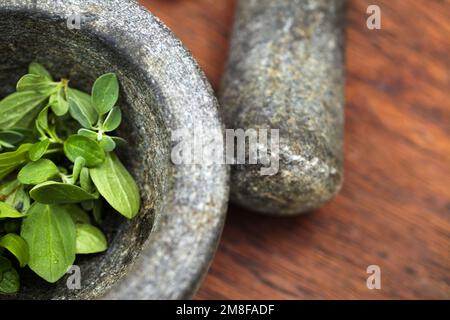 Pflanzen, Mörser und Stößel für Kräuter auf dem Tisch in der Küche. Gemüse, Lebensmittel und Geräte zum Zerkleinern von Basilikumblättern, Pflanzen oder Gewürzen für Stockfoto