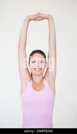 Sie lockert sich für ihr Workout. Eine junge Frau streckt ihre Arme über ihren Kopf. Stockfoto