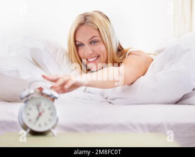 Aufwachen mit einem Lächeln. Eine attraktive junge Frau, die morgens ihren Wecker ausschaltet. Stockfoto