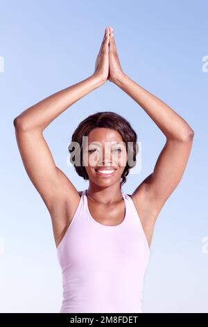 Zentriert und ruhig. Eine afroamerikanische Frau, die Yoga draußen vor blauem Himmel macht. Stockfoto