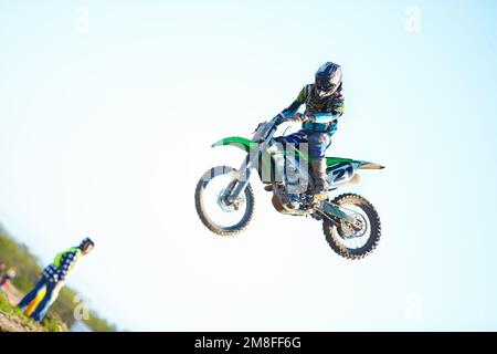 Sanfte Landung. Ein Motocross-Rennfahrer in der Luft mit einem Zuschauer im Hintergrund. Stockfoto