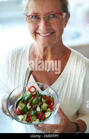 Köstlich und frisch. Gesunde Seniorin mit einer Glasschüssel gefüllt mit frischem Salat. Stockfoto