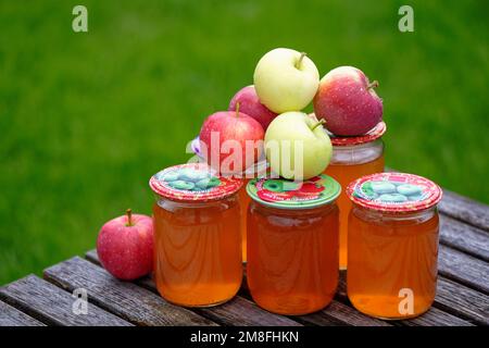 Frischer hausgemachter Apfelsaft in Glasgefäßen. Übersetzung russischer Aufschriften auf den Deckeln: „Rettung von Familienrezepten“ und „Gemüse aus dem Garten – Stockfoto