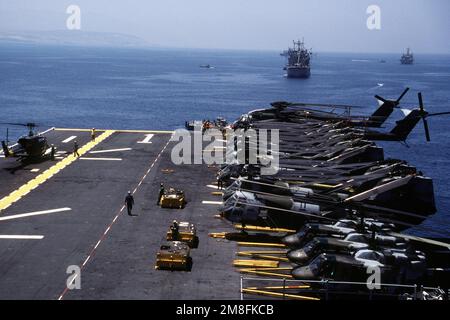 Die Besatzung des Flugdecks steht bei ihren Schleppern MD-3A an Bord des Amphibienschiffs USS WASP (LHD-1), während der Hubschrauber UH-1N Iroquois, Left, für den Flug vorbereitet ist. Auf der rechten Seite befinden sich UH-1N Iroquois, Vordergrund, CH-46E Sea Knight, Center und CH-53E Super-Hallion-Hubschrauber, die der Marine Medium Helicopter Squadron 162 (HMM-162) für ihren Einsatz im Mittelmeer mit der Marine Expeditionary Unit 26. (26. MEU) zugewiesen wurden. Land: Atlantik (AOC) Stockfoto