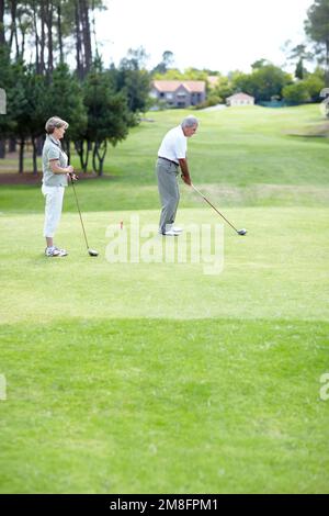 Dieses Spiel erfordert große Konzentration. Ein reifes Ehepaar, das eine Runde Golf spielt. Stockfoto