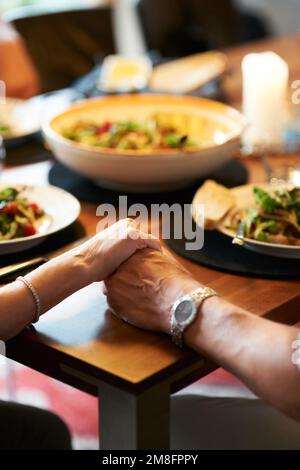 Lasst uns das Tischgebet sprechen... ein paar, die vor dem Essen Händchen halten. Stockfoto