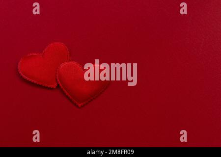 Hintergrund für Valentinstag-Design. Auf einem rot strukturierten Hintergrund sind 2 Herzen aus Satin. valentinstagskonzept, Platz für Text Stockfoto