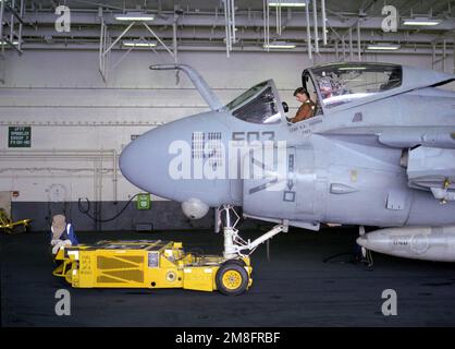 Ein Crewman, der ein SD-1D-Flugzeug besetzt, das einen Dolly beobachtet, wartet, während ein Schiffskamerad das Cockpit eines Angriffsgeschwaders 75 (VA-75) A-6E auf dem Hangardeck des Flugzeugträgers USS KITTY HAWK (CV-63) inspiziert. Land: Atlantik (AOC) Stockfoto