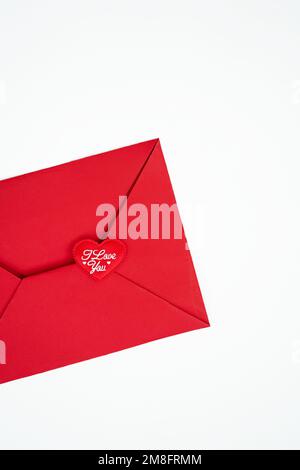 Auf weißem, vertikalem Hintergrund, einem roten Umschlag mit rotem Herz, auf dem weiß geschrieben ist Ich liebe dich Konzept Valentinstag Stockfoto