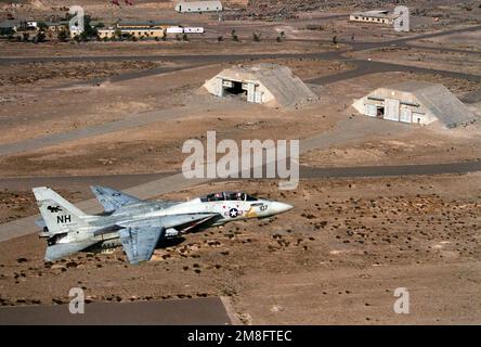 Ein Kampfgeschwader 114 (VF-114) F-14A Tomcat fliegt an einem gehärteten Flugzeughangar vorbei, der während der Operation Desert Storm beschädigt wurde. Betreff Betrieb/Serie: WÜSTENSTURMLAND: Kuwait (KWT) Stockfoto