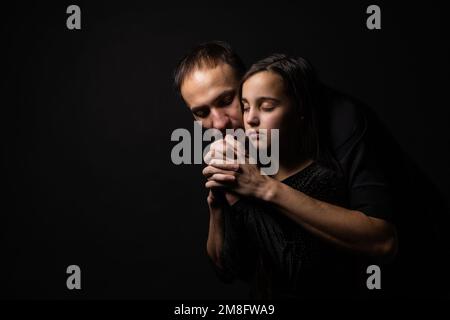 Junger Vater und Tochter beten mit Händen zusammen, mit Hoffnungsausdruck im Gesicht, sehr emotional und besorgt. Stockfoto