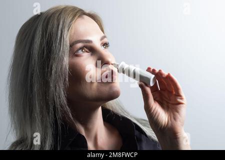 Frau, die Nasenspray auf hellem Hintergrund verwendet, Nahaufnahme Stockfoto