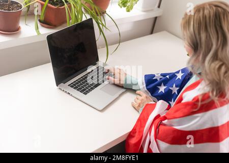 Positiver Lehrer im Headset, der Online-Unterricht auf einem Laptop in der Nähe von Flaggen in der Schule hat Stockfoto
