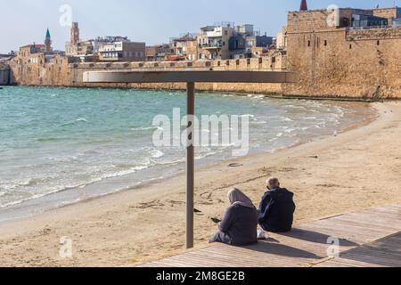 Acres, Israel - 08. Januar 2023: Blick auf den Pferdestrand, die Meereswand und den Fischereihafen bei Sonnenuntergang, mit Einheimischen und Besuchern, in der Altstadt von Acre Stockfoto