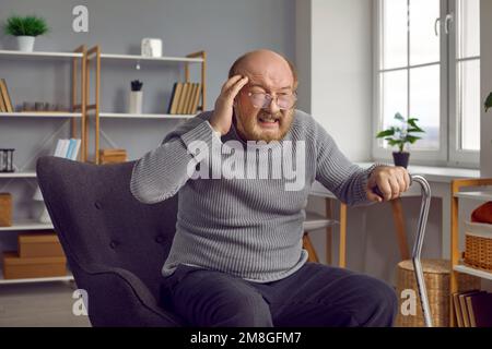 Gestresster Rentner mit Migräne sitzt zu Hause in seinem Sessel Stockfoto