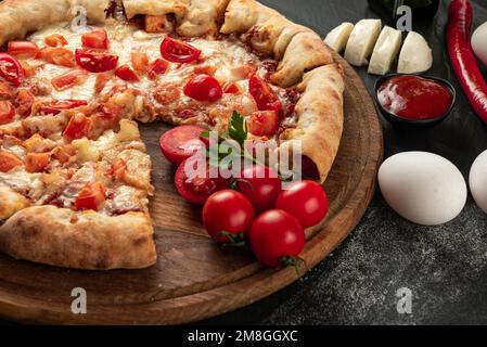 Zutaten für die Pizza auf dunklem Hintergrund. Indische Pizza mit Tomaten und Paprika aus nächster Nähe. Traditionelle indische Pizza auf Brot-Fladenbrot Stockfoto