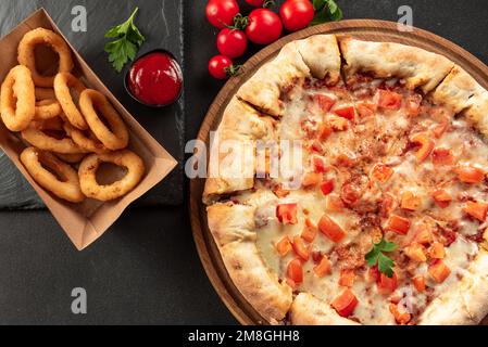 Indische Fladenbrotpizza auf dunklem Hintergrund. Indische Pizza auf dunklem Hintergrund mit Snacks. Indisches Fast Food-Set Stockfoto