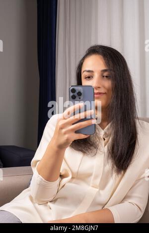 Online einkaufen, lächelnde, glückliche Frau, die ihr Smartphone online hält. Entspannen Sie sich zu Hause auf dem Sofa. Ich sitze auf der Couch. Schreiben, Lesen von Textnachrichten. Stockfoto