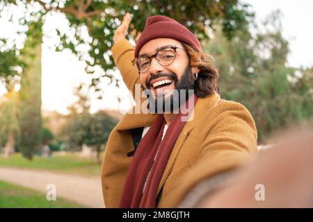 Glücklicher junger Kaukasier mit Brille und Bart, der im Winter im Park ein Selfie im Freien macht. Stockfoto