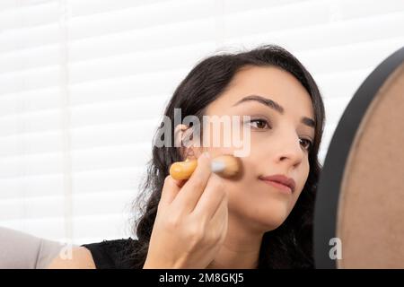 Nahaufnahme einer schönen Frau, die sich schminkt. Putzen Sie rotes oder beigefarbenes Fundament mit einer Bürste. Naturschönheit Konzeptfoto, Spiegel Stockfoto