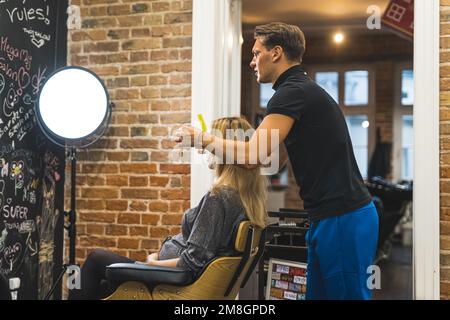 Schwangere Frau sitzt auf dem Stuhl und Friseur passt ihr Haar an, Salon, mittlere Volltreffer. Hochwertiges Foto Stockfoto