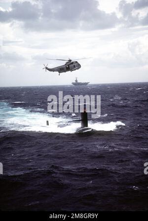 Ein Hubschrauber-U-Boot-Abwehrstaffel (HS-5) SH-3 Sea King Hubschrauber schwebt über dem nuklearbetriebenen Angriffs-U-Boot USS HAMMERHEAD (SSN-663), während er sich darauf vorbereitet, ein Geschenk des kommandierenden Offiziers des nuklearbetriebenen Flugzeugträgers GEORGE WASHINGTON (CVN-73), Hintergrund, an die Crew des HAMMERHEADS zu übergeben. Land: Atlantik (AOC) Stockfoto