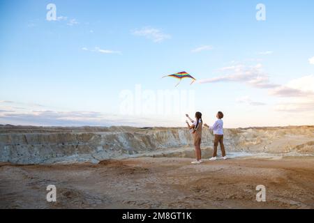 Ein Junge und ein Mädchen, die einen Drachen am Rand einer hohen Klippe stehen. Stockfoto
