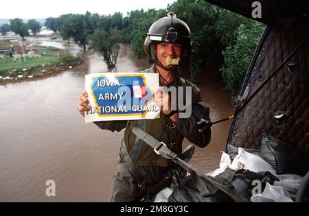 PERSONAL SGT. Fred Miller von der Army National Guard steht am Rand eines UH-1 Hubschraubers, während er ein Schild mit der Aufschrift „Iowa Army National Guard“ hält. Der Hubschrauber ist im Flug und das Hochwasser ist im Hintergrund zu sehen. (Genaues Datum unbekannt). Basis: Des Moines Staat: Iowa (IA) Land: Vereinigte Staaten von Amerika (USA) Stockfoto