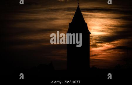 Die Silhouette eines Turms mit einer Kuppel, umgeben von Bäumen, bei Sonnenuntergang und Wolken Stockfoto
