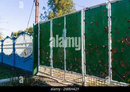 Auf Dem Land. Beschädigter Zaun in der Nähe des Hauses. Es gibt Löcher im Zaun von Kugeln und Muschelfragmenten. Krieg in der Ukraine. Russische Invasion der Ukraine Stockfoto