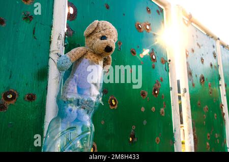 Auf Dem Land. Beschädigter Zaun in der Nähe des Hauses. Ein Spielzeug (Teddybär) hängt am Zaun (Nahaufnahme). Krieg in der Ukraine. Russische Invasion der Ukraine Stockfoto