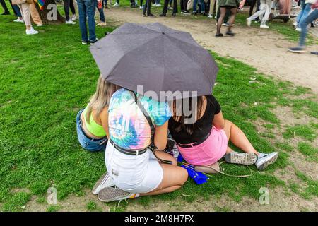 Junge Frauen versammelten sich unter demselben Schirm während einer unerwarteten Frühlingsschauerparty. Brüssel. Stockfoto