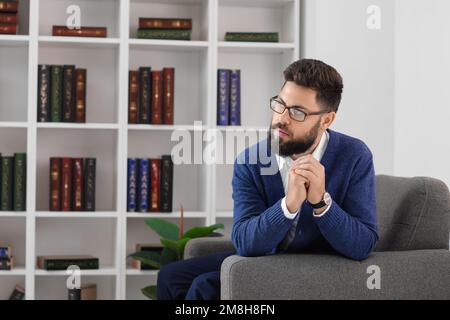 Ein aufmerksamer junger Mann mit Bart im Sessel zu Hause Stockfoto