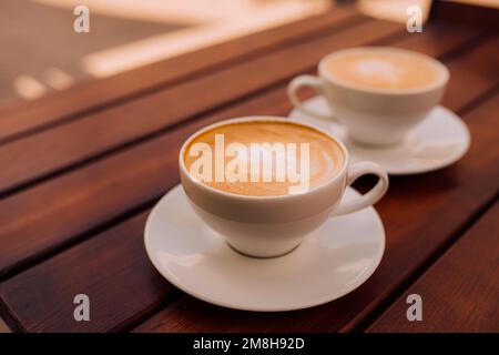 Zwei Tassen Cappuccino mit Latte Art auf dem Holztisch. Wunderschöner Schaumstoff und Keramikbecher Stockfoto