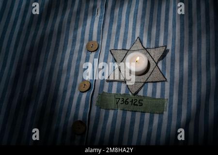 Brennende Kerze, jüdische Marke und Nummer auf der Uniform, Nahaufnahme. Internationaler Holocaust-Gedenktag Stockfoto