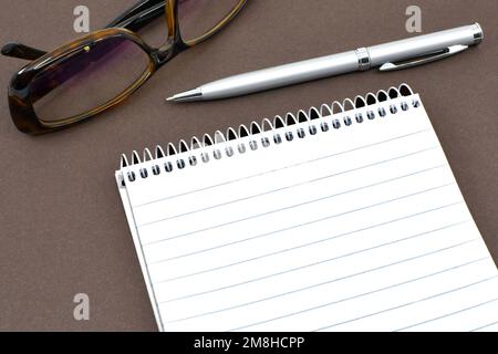Leerer Notizblock, Stift und Brille auf einfarbigem braunen Hintergrund. Bürokonzept. Stockfoto