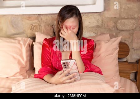 Eine Sinusitis haben. Asiatische Frauen im Nachthemd und nachts Kopfweh im roten Satinmantel. Stockfoto