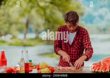 Ein Mann bereitet ein köstliches Abendessen für seine Freunde zu, die Spaß am Fluss in der Natur haben Stockfoto