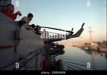 Die Besatzungsmitglieder beobachten von der Geländer aus den nuklearbetriebenen Flugzeugträger USS THEODORE ROOSEVELT (CVN-71), während das Schiff den Suezkanal auf dem Weg zum Roten Meer durchquert. Der Heck eines Marine Heavy Helicopter Squadron 362 (HMH-362) UH-1N Iroquois Hubschraubers ragt über die Seite des Flugzeugträgers. Staat: Suez Canal Country: Ägypten (EGY) Stockfoto