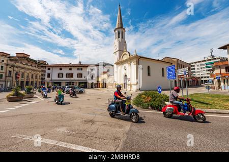 Kirche San Rocco mit dem Glockenturm, 1536. Spilimbergo, Pordenone, Friaul-Julisch Venetien, Italien. Gruppe von Radfahrern auf dem Piaggio Vespa Roller. Stockfoto