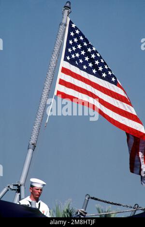 Während der Stilllegungszeremonie des Schiffes steht ein Matrose neben dem nationalen Fähnrich auf dem Heck der Fregatte USS LOCKWOOD (FF-1064). Basis: Marineflugstation, San Diego Bundesstaat: Kalifornien (CA) Land: Vereinigte Staaten von Amerika (USA) Stockfoto