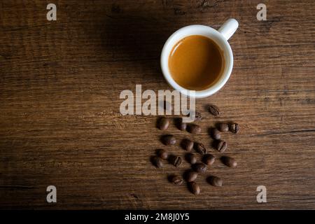 Weiße Tasse Espresso mit Kaffeebohnen auf einem Holztisch Stockfoto