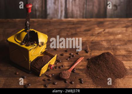 Kaffeemühle neben einem Löffel mit Kaffee, ein kleiner Berg gemahlenen Kaffees und Kaffeebohnen auf dem Holztisch Stockfoto