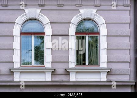 Zwei Bogenfenster in einem weißen Rahmen vor einer grauen Wand. Aus der Windows of the World-Serie. Stockfoto