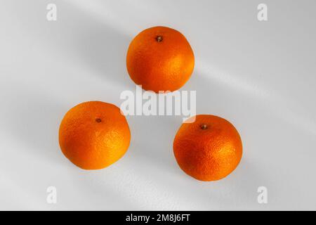 Drei leuchtend orangefarbene Tangerinen auf der weißen Oberfläche des Tisches. Stockfoto