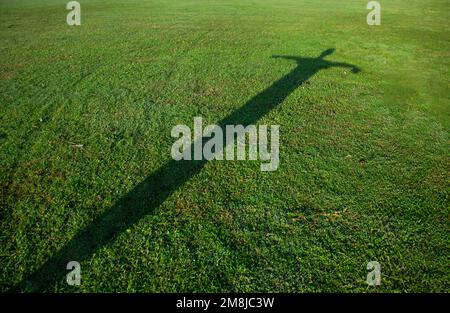 Silhouette des Menschen in Kreuzform auf grünem Gras Stockfoto